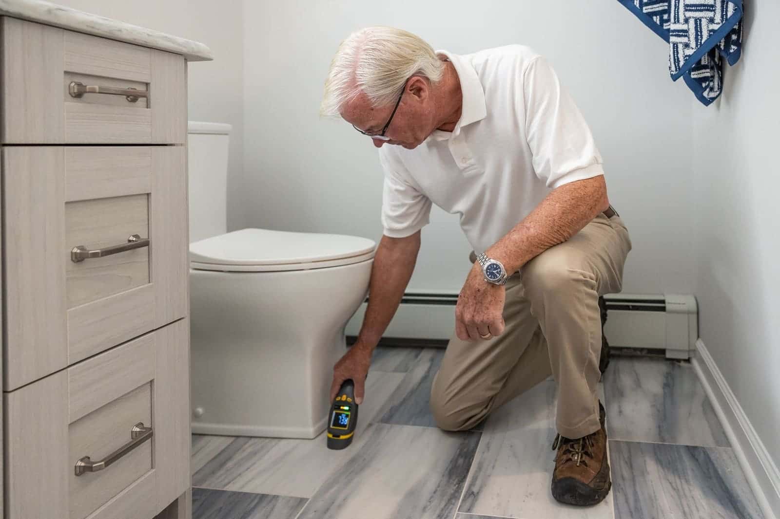 Man checking the floor beside a toilet with a handheld meter