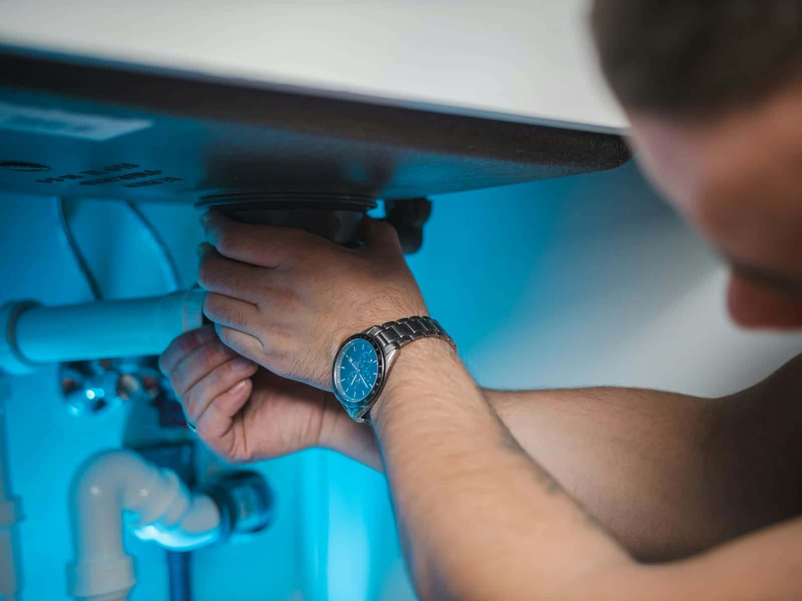 Hands tightening plastic drain fittings beneath a sink